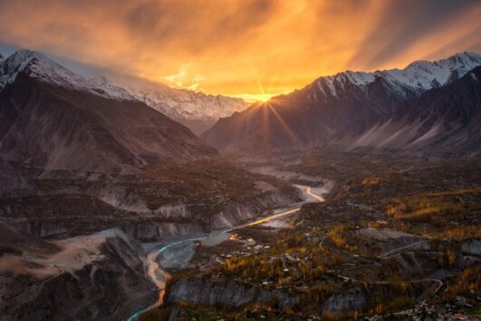 Breathtaking sunset over Hunza Valley, Pakistan, with golden rays illuminating the snow-capped mountains and river.