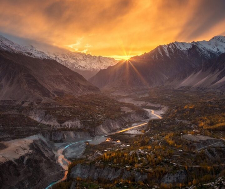 Breathtaking sunset over Hunza Valley, Pakistan, with golden rays illuminating the snow-capped mountains and river.