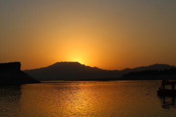 Scenic sunset over the Indus River with boats anchored near the shore, creating a peaceful atmosphere.