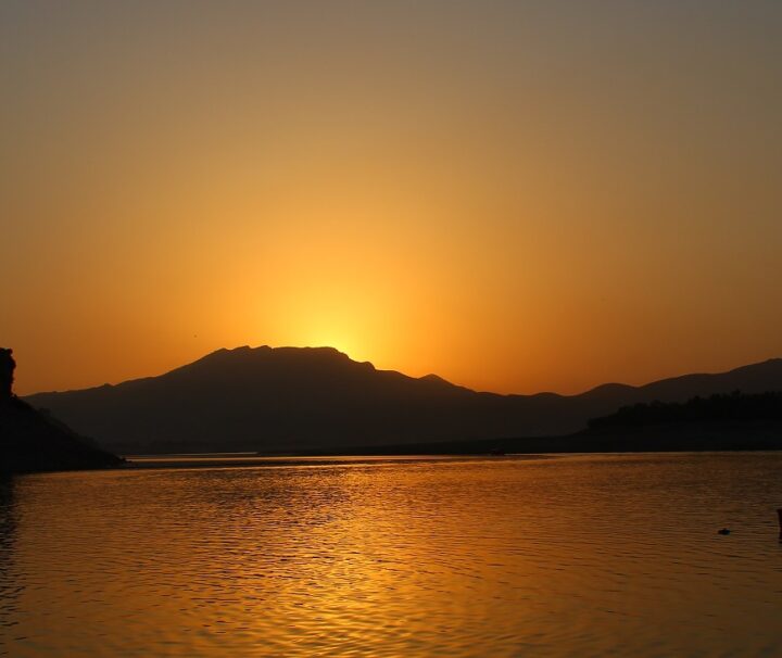 Scenic sunset over the Indus River with boats anchored near the shore, creating a peaceful atmosphere.