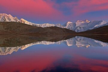 Rush Lake in Hunza reflecting snow-capped peaks under a stunning sunset sky.